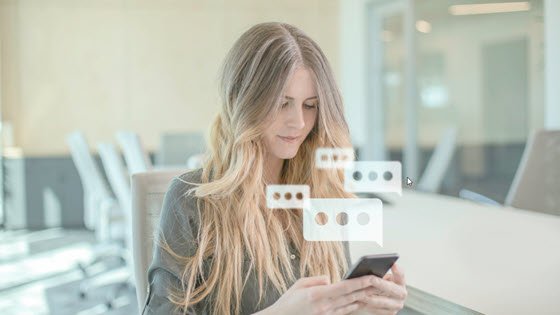 sms marketing hero image - a young woman with long blond hair looks at her phone and 3-dot sms text bubbles appear above it