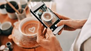 a woman holds a phone and takes an aesthetic photo of her coffee cup to illustrate an ideal social media feed