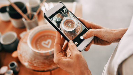 a woman holds a phone and takes an aesthetic photo of her coffee cup to illustrate an ideal social media feed